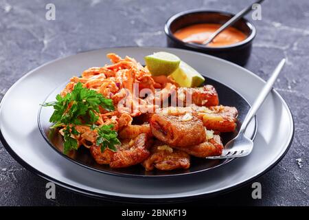 Cucina caraibica: Piatti fritti serviti con pollo sminuzzato caricato con salsa di bufalo, serviti con lime e prezzemolo su un piatto nero con forchetta, Foto Stock