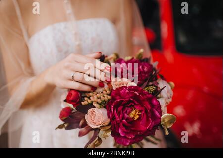 Primo piano bouquet sposa, il bouquet è composto da rosa peonie rosse. La sposa tiene il bouquet, ha una manicure rossa, un anello di diamante sul suo anello fi Foto Stock