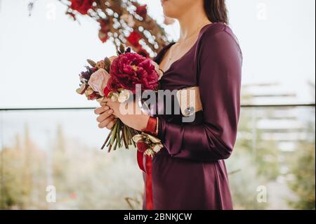 Primo piano bouquet sposa, il bouquet è composto da rosa peonie rosse. La ragazza tiene il bouquet e il telefono sotto l'ascella Foto Stock