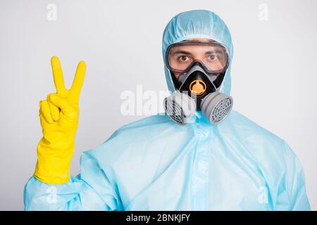 Ritratto di un uomo medico in bianco maschera di respirazione uniforme rendere V-segno isolato su sfondo grigio Foto Stock