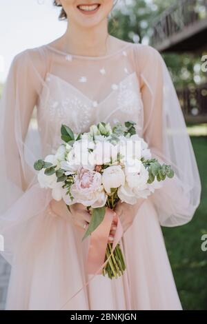 Primo piano bouquet sposa, il bouquet è composto da peonie bianche e rosa, eucalipto. La sposa vestita con abito da sposa rosa tiene il bouquet Foto Stock