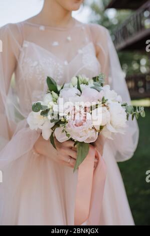 Primo piano bouquet sposa, il bouquet è composto da peonie bianche e rosa, eucalipto. La sposa vestita con abito da sposa rosa tiene il bouquet Foto Stock