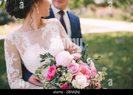 Primo piano di un bouquet di peonie, rose, eucalipto in tonalità bianco-rosa legato a nastri rosa. La sposa tiene un bouquet in mano in un wh Foto Stock