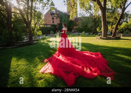 Bella donna tattoed rosso in lungo vestito rosso che posa vicino al castello Foto Stock