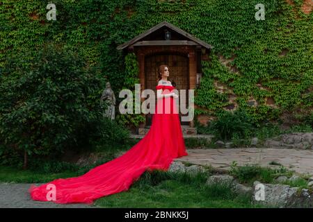 Bella donna tattoed rosso in lungo vestito rosso che posa vicino al castello Foto Stock