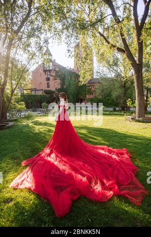 Bella donna tattoed rosso in lungo vestito rosso che posa vicino al castello Foto Stock