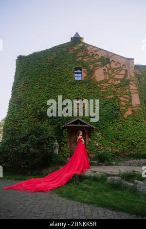 Bella donna tattoed rosso in lungo vestito rosso che posa vicino al castello Foto Stock