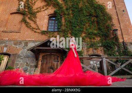 Bella donna tattoed rosso in lungo vestito rosso che posa vicino al castello Foto Stock