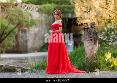 Bella donna tattoed rosso in lungo vestito rosso che posa vicino al castello Foto Stock