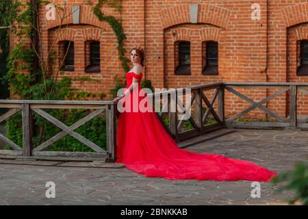 Bella donna tattoed rosso in lungo vestito rosso che posa vicino al castello Foto Stock