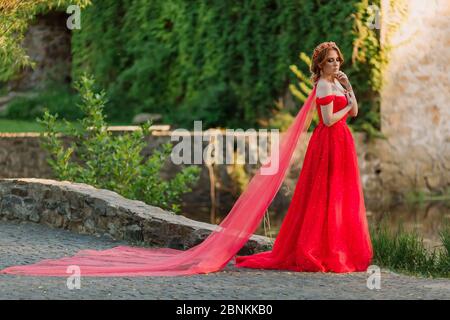 Bella donna tattoed rosso in lungo vestito rosso che posa vicino al castello Foto Stock