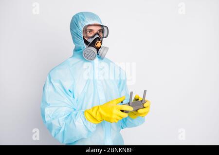 Foto del medico uomo tenere il joystick di controllo volante drone indossare Hazmat vestito giallo lattice guanti di gomma occhiali di protezione maschera di respirazione isolato su colore grigio Foto Stock