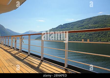 Ponte di una nave mentre naviga lungo il fiordo bello con le montagne e i vilages lungo l'acqua, Hardangerfjord, Norvegia. Foto Stock