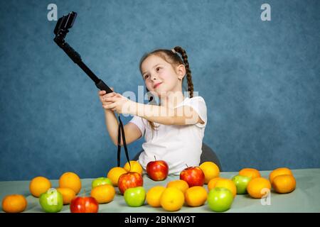 Bambina gioca con frutta e prende un selfie al telefono. Vitamine e nutrizione sana per i bambini. Foto Stock