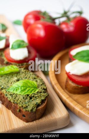 Bruschetta tradizionale italiana: Toast con salsa al pesto al basilico, mozzarella e pomodori sulla tavola di legno circondata da l basilico Foto Stock