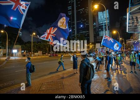 I manifestanti pro-democrazia hanno fatto ondere le vecchie bandiere coloniali della città durante una veglia fuori dal centro commerciale Pacific Place nella zona dell'Ammiragliato di Hong Kong per celebrare il 11 mese anniversario da quando un uomo è caduto alla sua morte da un ponteggio, Durante una protesta contro il disegno di legge sull'estradizione del governo di Hong Kong lo scorso anno. Foto Stock