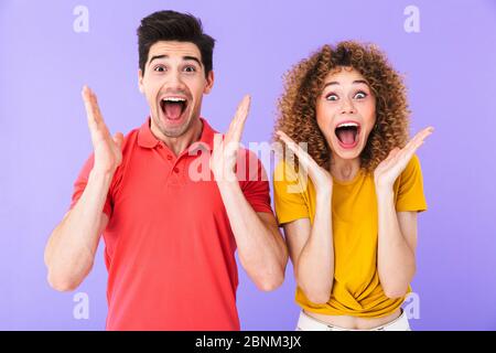 Ritratto di felice uomo e donna caucasica in abiti di base urlando mentre si gettano le braccia a macchina fotografica isolata su sfondo viola Foto Stock