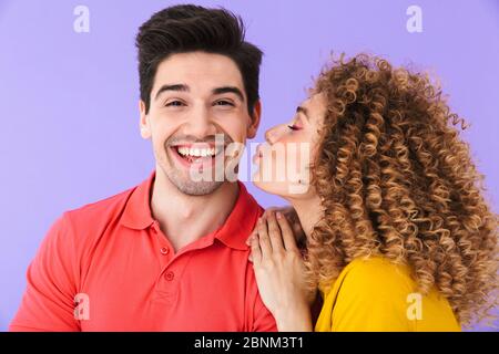 Ritratto di giovane uomo felice sorridente mentre bella donna baciando sulla guancia isolato su sfondo viola Foto Stock