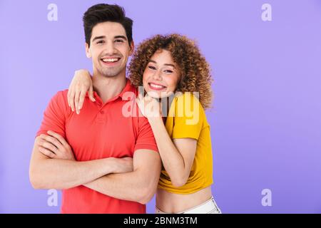 Ritratto di gioioso popolo caucasico uomo e donna in abiti di base sorridenti e abbraccianti insieme isolati su sfondo viola Foto Stock