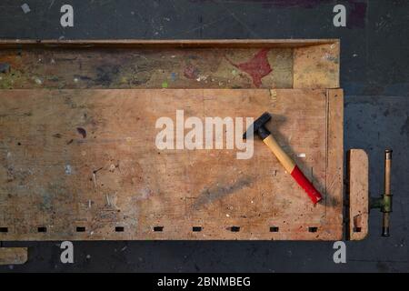 banco da lavoro in legno antico, fotografato graficamente dall'alto, pavimento in officina grigio scuro, con martello, in ordine, variante 3 di 5 Foto Stock