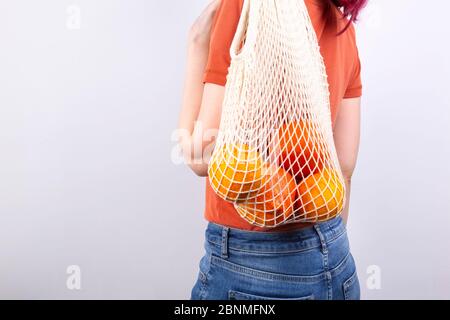 Giovane donna in jeans blu e T-shirt arancione è su borse a corda con vari agrumi su sfondo grigio. Concetto zero sprechi, eco-compatibile. Centro benessere copie Foto Stock