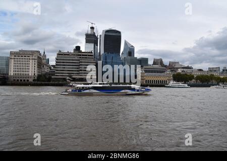 Una nave/barca blu che scende lungo il Tamigi a Londra, Inghilterra, Regno Unito. Passando davanti ad alcuni famosi edifici iconici, tra cui l'edificio Walkie Talkie Foto Stock