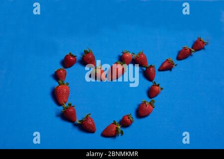 Cuore fatto di fragole su sfondo blu. Colori della natura Foto Stock