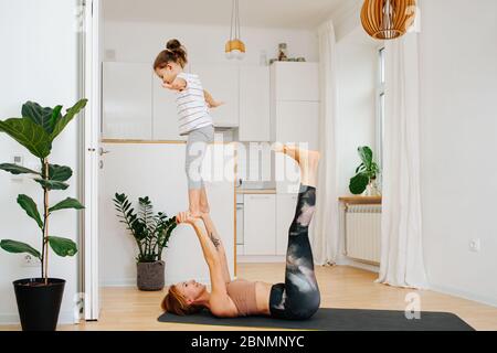 Mamma che fa ginnastica con la figlia a casa, ragazza che si trova sulle sue braccia Foto Stock