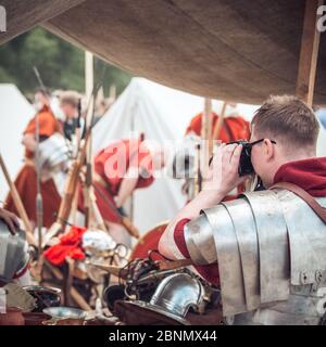 Un uomo in armatura di un guerriero legionario romano fotografa i suoi amici in una festa di reenattori Foto Stock