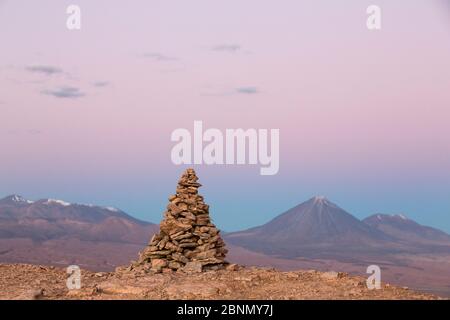 Apacheta / Apachita - un cairn di pietra nelle Ande, un piccolo mucchio di rocce costruito lungo il sentiero in alta montagna con il vulcano Licancabur (5916 m a. Foto Stock