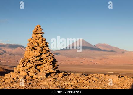 Apacheta / Apachita - un cairn di pietra nelle Ande, un piccolo mucchio di rocce costruito lungo il sentiero in alta montagna con il vulcano Licancabur (5916 m a. Foto Stock