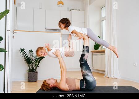 Mamma che fa ginnastica con i suoi figli su un tappetino yoga a casa Foto Stock