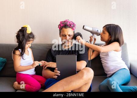 Le figlie graziose stanno dipingendo le unghie e pettinando i capelli del loro bel giovane padre Foto Stock