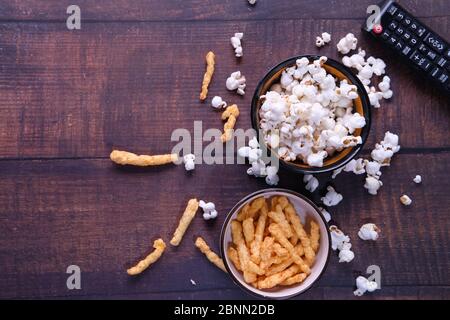 Vista dall'alto di una ciotola di popcorn, patatine e telecomando tv su sfondo di legno Foto Stock
