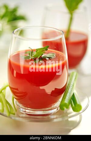 Succo di pomodoro su un piatto bianco con una guarnitura di sedano e prezzemolo. Concetto di alimentazione sana. Foto Stock