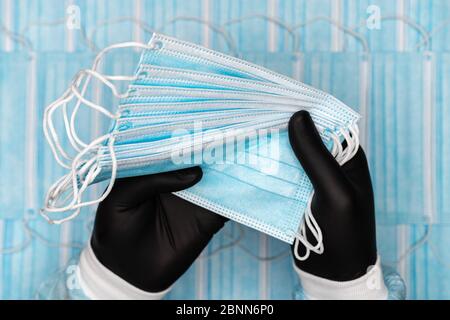 Gruppo di tenuta infermiere blu chirurgico maschere mediche viso in nero guanto protettivo in due mani. Immagine concettuale su fondo lotto di bende di protezione Foto Stock