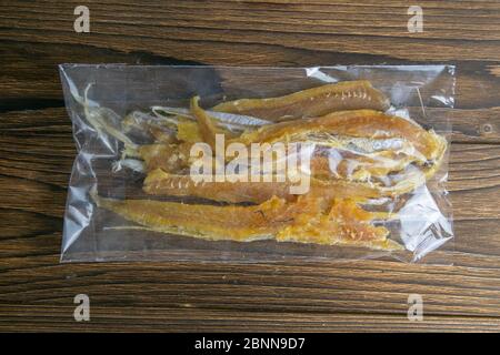 Filetto di tonno essiccato in un pacchetto trasparente antipasto su sfondo di legno di béron. Snack Pesce alla birra. Primo piano Foto Stock