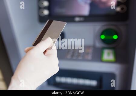 Porta con te un guanto medico protettivo che tiene la carta di credito accanto al bancomat. Concetto Covid-19. Foto Stock