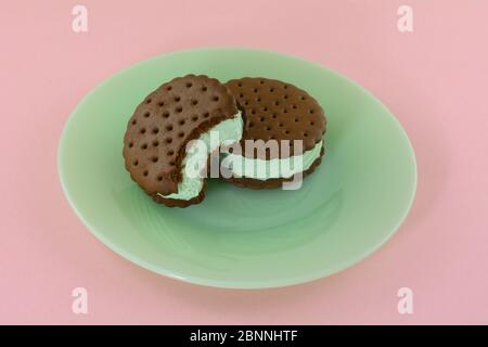 Panini con gelato alla menta con un boccone mancante sul piatto da dessert verde su sfondo rosa Foto Stock