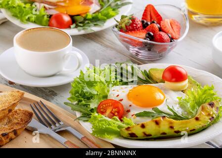 Colazione salutare con uova fritte, avocado, pomodoro, toast, caffè e succo d'arancia su sfondo di legno. Concetto di colazione europea o americana. Clos Foto Stock