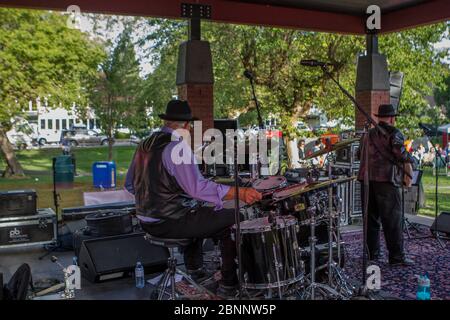 Senior maschio, vestito con abiti acutamente, con fedora Hat, suonando batteria, in rock band al concerto di outoor. Foto Stock