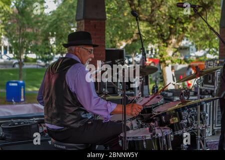 Senior maschio, vestito con abiti acutamente, con fedora Hat, suonando batteria, in rock band al concerto di outoor. Foto Stock