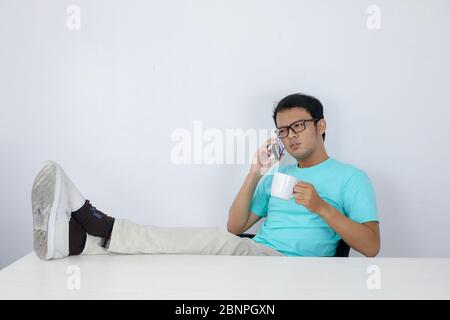 Il giovane asiatico ha scioccato quando ha guardato lo smartphone con la gamba sul tavolo Foto Stock