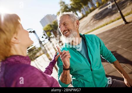 Sportivo felice uomo maturo discutere qualcosa con sua moglie mentre si esercita insieme nella mattina presto, coppia senior facendo sport all'aperto e. Foto Stock