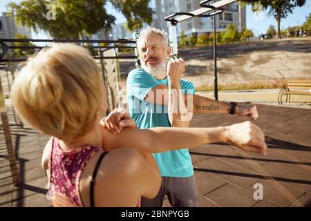 Fisicamente attivo in qualsiasi età. Coppia di famiglia matura atletica in abbigliamento sportivo facendo esercizi di stretching nella mattina presto all'aperto, coppia anziane fare Foto Stock