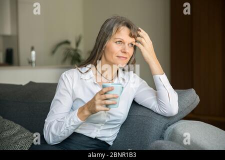 Donna di mezza età in contesti formali ware tenendo una tazza di caffè nel suo appartamento di città Foto Stock