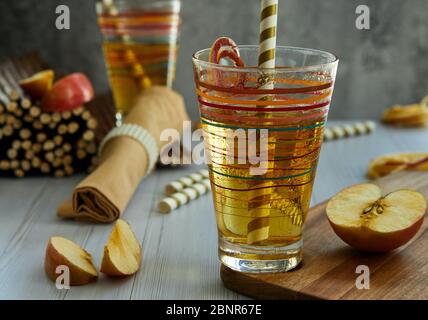 Succo di mela fresco in un bicchiere, paglia, mele rosse su un tavolo di legno. Foto Stock