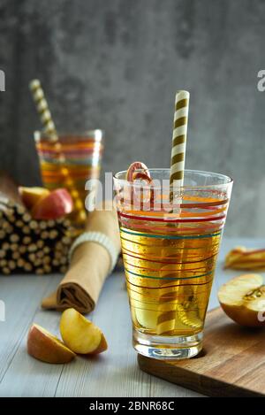 Succo di mela fresco in un bicchiere, paglia, mele rosse su un tavolo di legno. Foto Stock