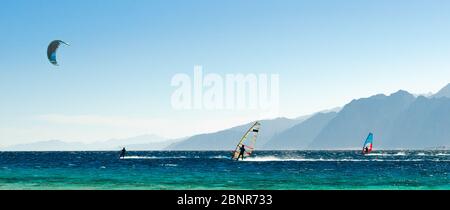 Surfisti e kitesurfisti ride in Mar Rosso sullo sfondo della costa rocciosa in Egitto Dahab Foto Stock