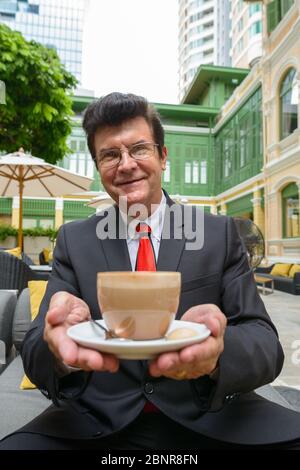 Uomo d'affari felice maturo che tiene una tazza di cappuccino caffè Foto Stock